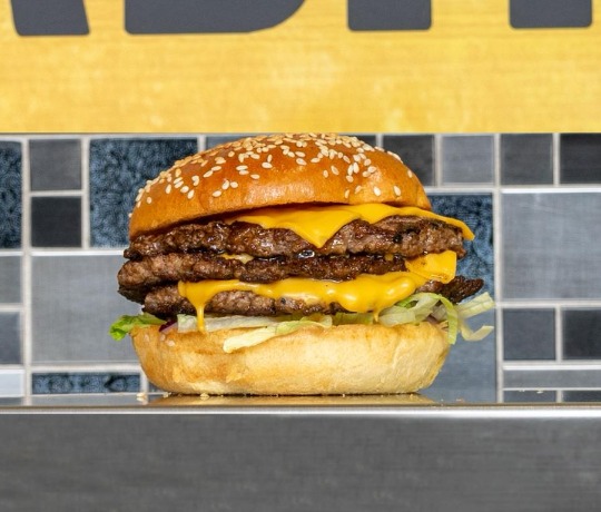 Crispy chicken burger in a bun sat on a wooden board with onion, rocket and crispy batter